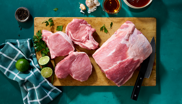 Raw pork chops and pork shoulder on a cutting board with knife, lime, garlic, spices, and marinades