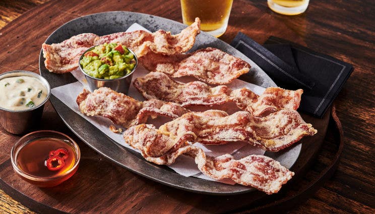 Crispy bacon strips with guacamole, dipping sauces on a rustic serving tray